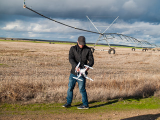 A drone pilot configuring his drone in a field with and irrigation system before flying
