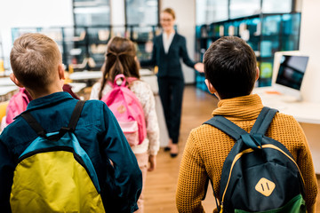 back view of schoolkids with backpacks looking at librarian in library