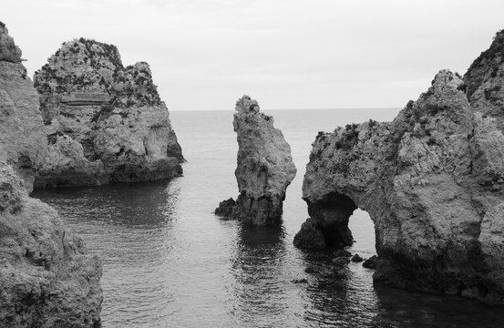 Unique stone arches, caves, rock formations at Dona Ana Beach (Lagos, Algarve coast, Portugal) in the evening light. Black white photo.