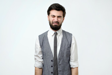 Young hispanic man in vest and shirt crying because he should work on holidays. Negative human emotion.
