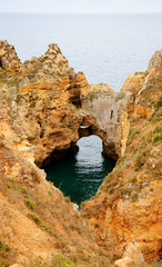 Ocean water seen through hole in rocks. Stone arches, caves, rock formations at Dona Ana Beach (Lagos, Algarve coast, Portugal) in the evening light.