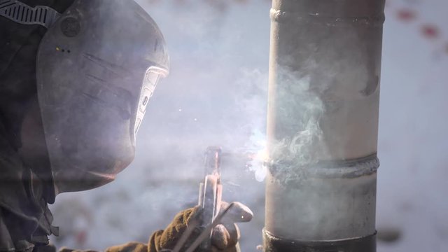 welder is welding pipes outdoors in winter day, he is using manual instrument, flashes are lighting