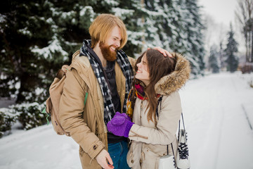 Date of the young couple in the winter. Young Caucasian man with a beard and long hair fooling around kid snow snowballs with a woman, winter games Valentine's Day in the snowy woods