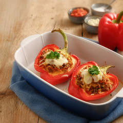 stuffed red bell pepper baked with cheese in a blue casserole dish on a rustic wooden table,