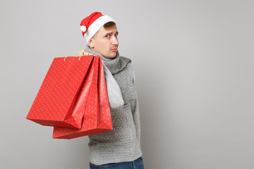 Young Santa man in Christmas hat holding red package bag with gifts, purchases after shopping isolated on grey background. Happy New Year 2019 celebration holiday party concept. Mock up copy space.