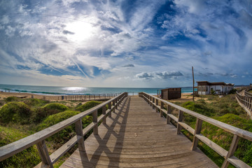Fototapeta na wymiar Wooden walkways lead to water in famous beach of Tres Irmaos in Alvor, Portimão, Algarve, Portugal, Europe. Praia dos Tres Irmaos. The sun shines through the clouds, the waves roll on the sand.