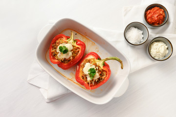 stuffed red bell pepper with cheese au gratin in a blue casserole dish on a white table, copy space, high angle view from above