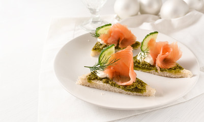 festive canapes with smoked salmon on a plate on a white table with christmas decoration, large copy space