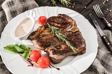 Grilled pork chop steak with rosemary, tomatoes and spices on plate over wooden rustic background. Hot Meat Dishes. Top view, flat lay