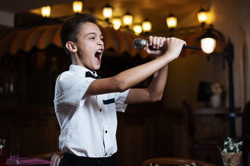 Boy in a white shirt singing into the microphone in a restaurant. baby karaoke.