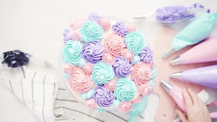 Flat lay. Piping pastel color buttercream rosettes on a white cake to make a unicorn cake.