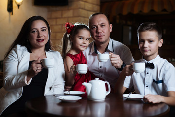 Family came together in a cafe. Mom, dad, little daughter and son drink tea. They are happy together. Happy family lunch concept.