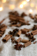 Cinnamon sticks and anise on beige tablelcloth. Fairy lights in the background. Selective focus.