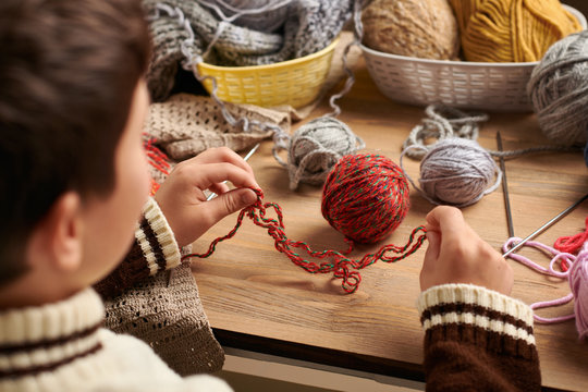 Child boy is learning to knit. Colorful wool yarns are on the wooden table. They are placed as smiling face. Hand closeup.