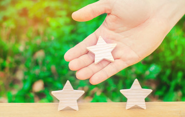 The hand stretches the third star to the other two. The concept of recognition of high quality and good service. Review hotel or cafe. High rating, success and achievement. Promotion.