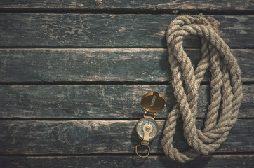 Compass and a mooring rope on aged wooden table background with copy space.