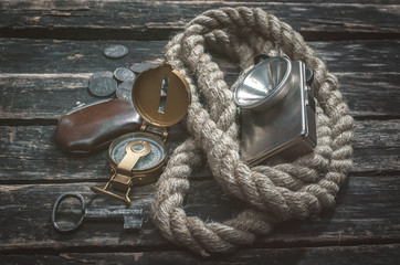 Compass, wallet, coins, rope, flashlight and a key of treasure chest on aged wooden adventurer or...