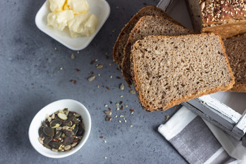 Sliced whole wheat bread baked with seeds and butter on wooden cutting board. Simple breakfast.