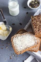 Sliced whole wheat bread baked with seeds and butter on wooden cutting board. Simple breakfast.