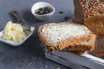 Sliced whole wheat bread baked with seeds and butter on wooden cutting board. Simple breakfast.