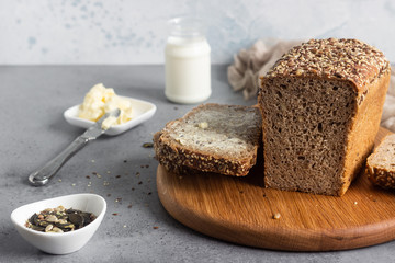 Sliced whole wheat bread baked with seeds and butter on wooden cutting board. Simple breakfast.