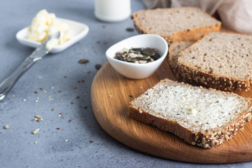 Sliced whole wheat bread baked with seeds and butter on wooden cutting board. Simple breakfast.