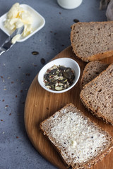 Sliced whole wheat bread baked with seeds and butter on wooden cutting board. Simple breakfast.