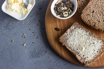 Sliced whole wheat bread baked with seeds and butter on wooden cutting board. Simple breakfast.
