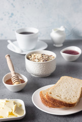 Butter and bread for breakfast with cup of coffee, granola, honey and jam over grey stone background. 