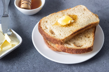Slices of toast bread and butter with honey on grey stone background
