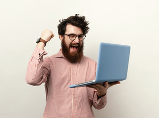 Winner bearded man wearing glasses and looking at screen and making a winner gesture