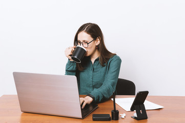 Portrait of a pretty youg woman sitting at the table, working on lapotop and drikining coffee