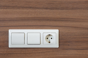 Two Modern Light Electrical Switches And One Socket For Connecting Electrical Appliances On Dark Wood Background.