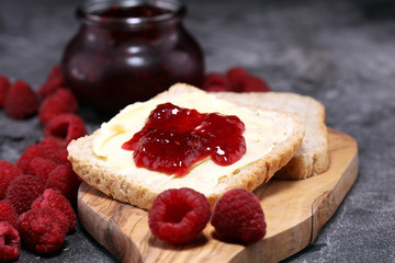 Toast bread with homemade raspberry jam or marmalade on rustic table served with butter for breakfast or brunch