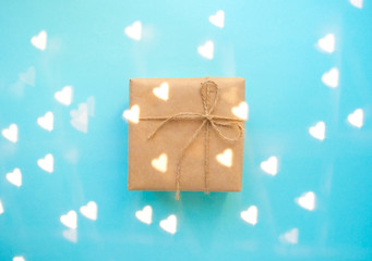 Gift box wrapped in brown colored craft paper and tied with tope on blue background with lights of heart shape.