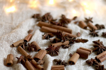 Cinnamon sticks and anise on beige tablelcloth. Fairy lights in the background. Selective focus.
