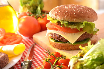 Homemade burger on cutting board with ingredients in kitchen