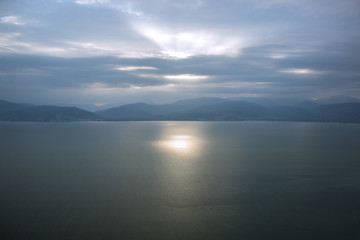 Obraz premium morning sun rise foggy weather scenic time of sea calm water surface and mountain horizon background silhouettes wallpaper pattern concept with empty space for copy or your text