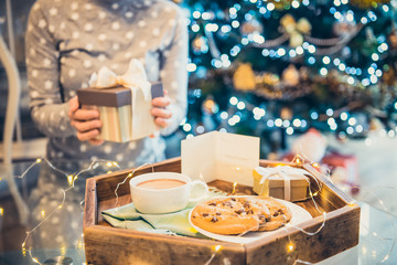 No face young woman opening Christmas present box with blurred wooden tray with festive breakfast. Cocoa and cookies for Santa. Christmas and New Year background. Soft selective focus. Vintage tonning