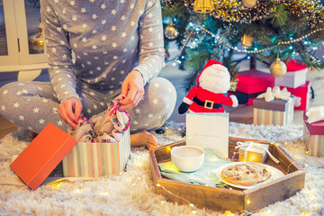 No face young woman opening Christmas present box with blurred wooden tray with festive breakfast. Cocoa and cookies for Santa. Christmas and New Year background. Soft selective focus. Vintage tonning