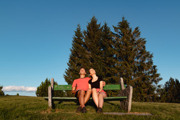 Couple sitting on bench in the mountains watching the sunset and taking a tan