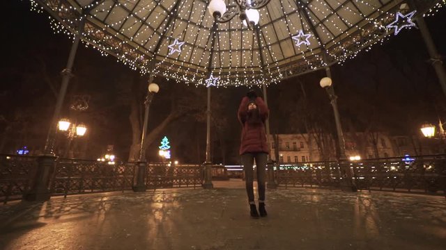 Young beautiful woman walks at night in the city, photographs Christmas decorations. Preparation for celebrating the new year