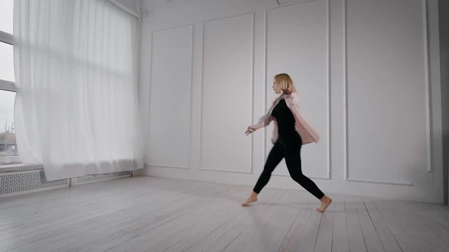 young pretty blonde woman is rehearsing her dance performance in white dancing hall, jumping and rotating