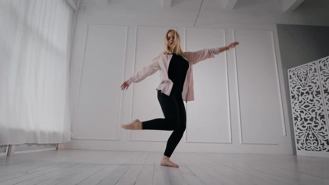 blonde woman is dancing contemporary performance in training hall, in daytime alone, rising legs up and spinning