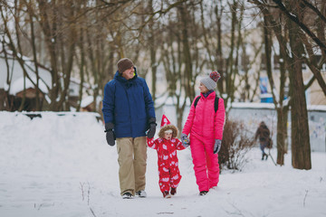Fototapeta na wymiar Happy family woman, man and little girl in winter warm clothes walking in snowy park or forest outdoors. Winter fun, leisure on holidays. Love childhood relationship family people lifestyle concept.