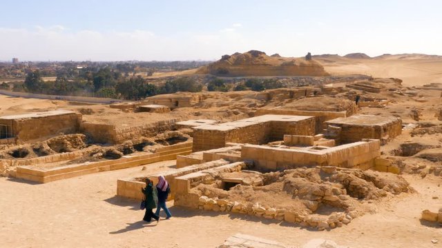 Two Egyptian women walking by the Giza complex with some mastabas