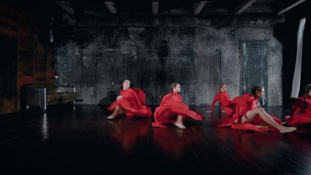 teenage girls are performing dance in a rehearsal room, wearing red dresses, leaping and whirling