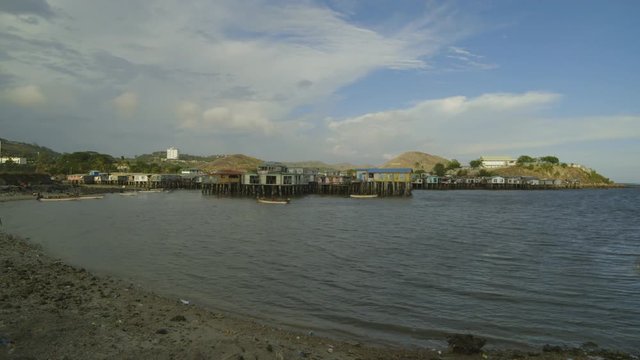 Wide still shot of stilts houses, canoes, horizon port buildings and hilly landscape, Port Moresby.
