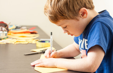 A young boy sat at a table making crafts with paper and a pen