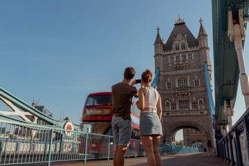 couple is taking a picture of a red double decker bus on the tower bridge in London